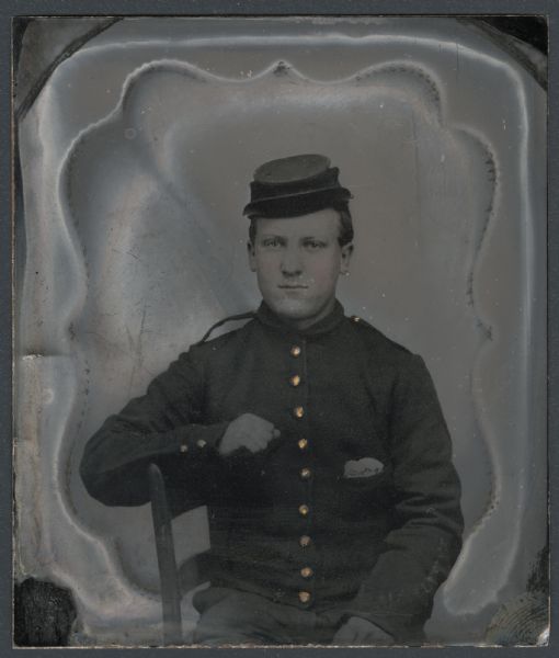 Ferrotype/tintype of George G. Burr in a Civil War uniform and cap. Waist-up portrait, seated sideways in a chair, with his arm on the back of his chair. Hand-coloring on cheeks, and gold details on buttons. 