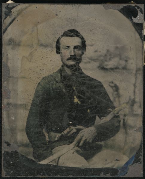 Ninth plate ferrotype/tintype of a waist-up portrait of a man identified only as Fox. He is seated, facing forward, wearing a short blue jacket, cradling a sword in his arm, with a gun tucked into his belt. Indistinguishable studio backdrop. Hand-coloring on jacket, cheeks, and gold details on buttons and hilt of sword. 