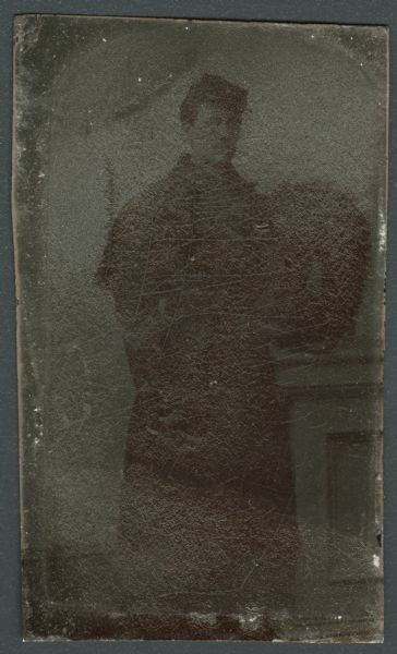 Ferrotype/tintype of John S. Skelton. Three-quarter length portrait of him standing in military uniform. Skelton was a corporal of the Old Milwaukee Light Guard. 