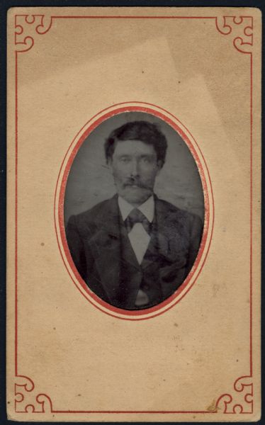 Ferrotype/tintype of a quarter-length portrait of Henry Arnold, son of Andrew Arnold. He is wearing a suit coat, vest, white shirt, and necktie, and has a moustache. Hand-coloring on cheeks.