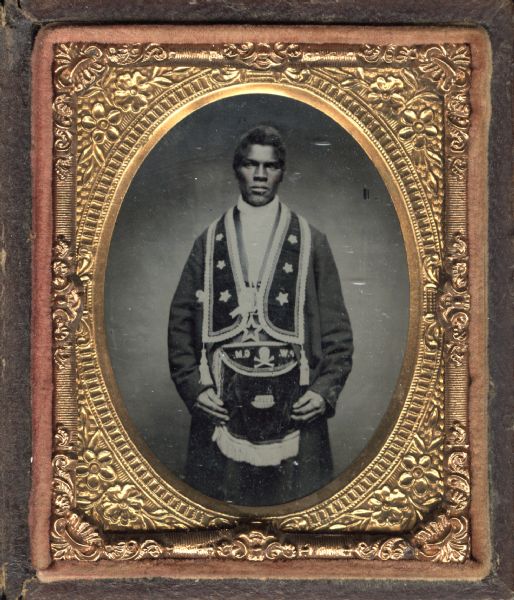 Ninth plate ambrotype of unidentified African-American man. Three-quarter length portrait, standing, facing forward. He is wearing a jacket over which hangs a stole and apron with star, skull & crossbones, and initials P.W. and G.M. [C.M.?], probably Masonic accoutrements. Hand-coloring on cheeks. 