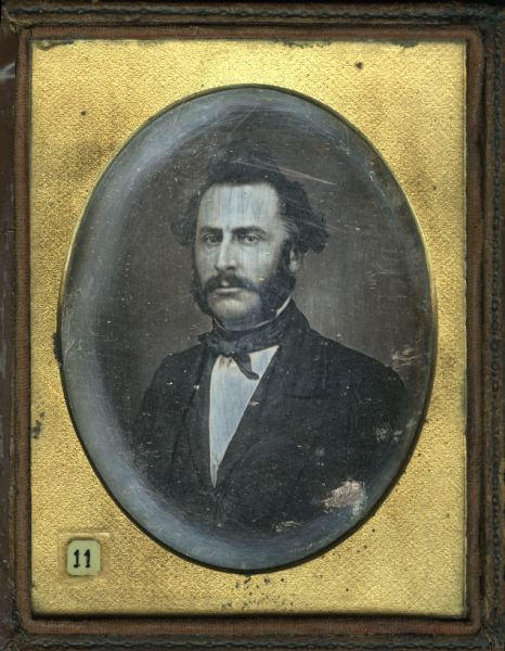 Quarter plate daguerreotype of Dr. Daniel Derendorf. Quarter-length portrait, facing slightly left, gaze forward. He is wearing a suit, cravat, and stand collar, with large sideburns, mustache, and his hair in a topknot. 