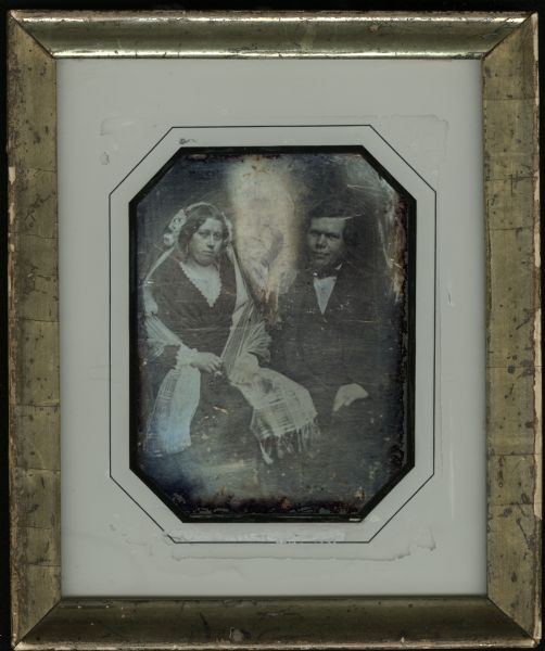 Quarter plate daguerreotype of Caspar William [Wilhelm(?)] Burmeister and Elise Thimm Burmeister on their wedding day, February 21, 1851. They are seated, turned slightly toward each other, and facing forward. Caspar is wearing a suit and small bow tie, and his hand is on his lap. Elise is wearing a bridal veil, a dark dress with the low neckline trimmed in white lace, and a plaid fringed shawl. 