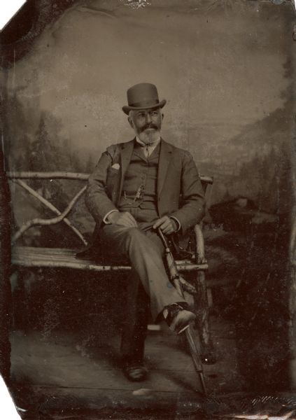 Ferrotype of Frederick Layton posing on a bench holding an umbrella in front of a painted background. Frederick Layton was the son of a Milwaukee butcher and ran the business until his retirement. He used his fortune to build the Layton Art Gallery and also contributed to the Layton Home for Incurables.
