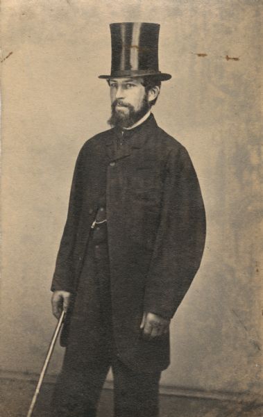 Three-quarter length portrait of Frederick Layton aged about 35. He is wearing a top hat and holds a walking stick.