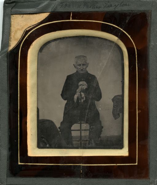 Ambrotype portrait of James Layton, collodian on glass plate set in a glass/ceramic frame with a gray tape edge binding. He is shown in late middle age seated with a cane propped between his knees. Written on both the front and back of the portrait are the words "Grandfather" or "Grand Father James Layton."