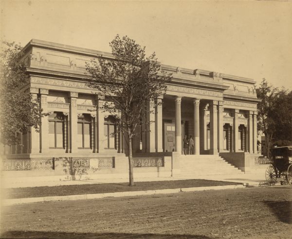 View across street towards the facade of the original Layton Art Gallery building at 758 N. Jefferson Street. Two men stand at the top of the stairs between the columns framing the entrance.