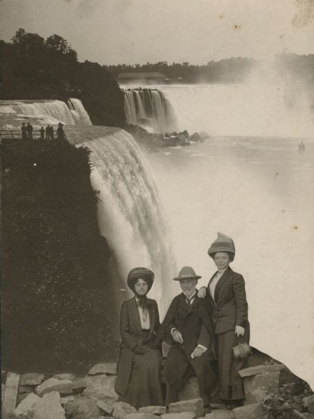 Frederick Layton posing in a studio shot with two women, one of whom is Laura Ackroyd. The backdrop is a photograph of Niagara Falls.