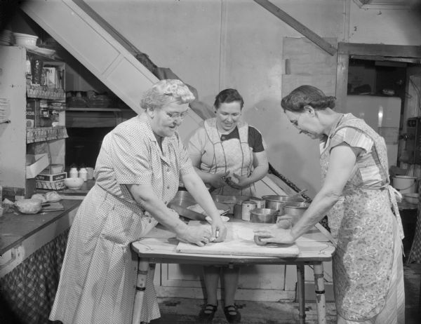 Three women stand at a table while making Cornish pasties in the kitchen of a small restaurant.