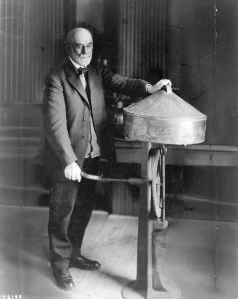 Interior full-length portrait of Dr. S.M Babcock and his tester for the separation of milk fat, which is a hand-cranked dairy centrifuge.