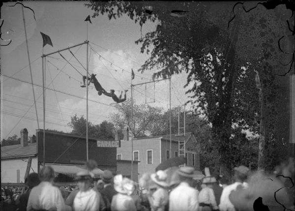 View from crowd of a pair of trapeze acrobats performing at a street fair.