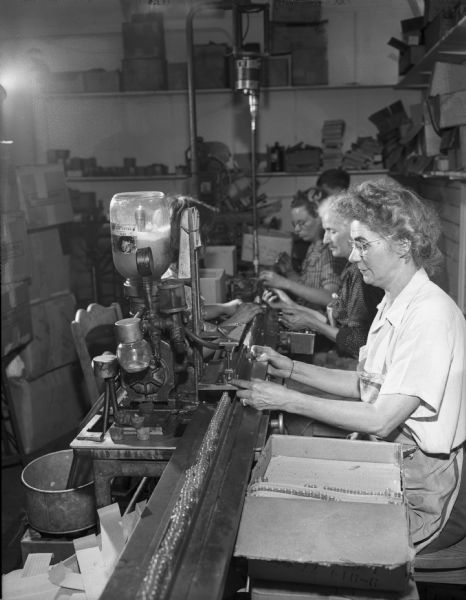 View from side of women sitting in a row working on an assembly line in a perfume factory.