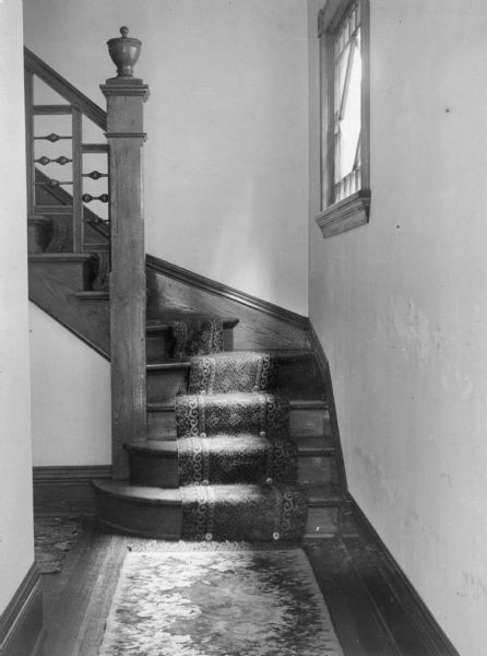 An interior view of the Henry Schildhauer residence on West Washington Avenue. Henry Schildhauer was the Chief Department of Revenue Collector. A curved, wooden staircase with decorative stair runner leads to the second floor of the house.