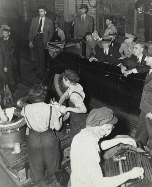 Presidential Tour - Series IV. Official party views women at work in Allis Chalmers factory.<p>President Franklin D. Roosevelt is looking through rear window while Governor Julius Heil, Wisconsin applauds. Walter Geist, Allis Chalmers president, seated near President, with James White, Allis Chalmers works manager in the front seat.<p>Surprise censored visit which the press were allowed to report in early October, by the N.Y. Times.