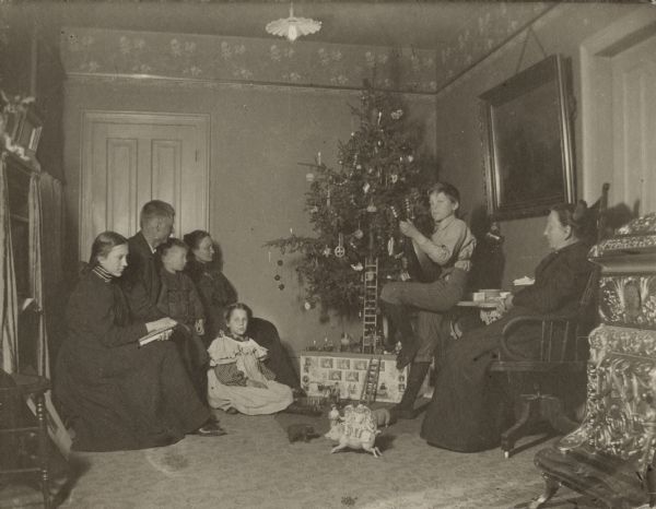 A family, two parents and five children, gathered around a decorated Christmas Tree with gifts underneath.