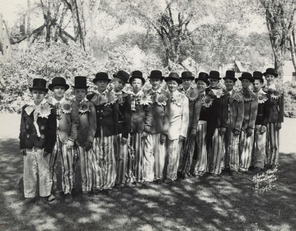 Lakewood School students, costumed for various performances under the general title "The Peoples of Wisconsin" given in connection with the Wisconsin Centennial. All the boys are wearing bowler hats, striped pants, and paper sunflowers in their lapels.