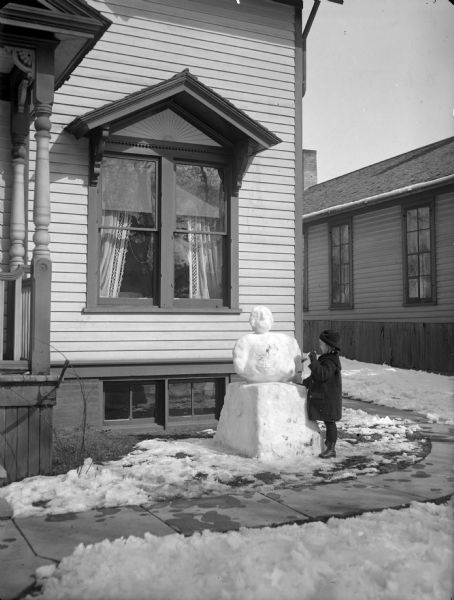 A child building a snowman in front of the Herman Taylor home.