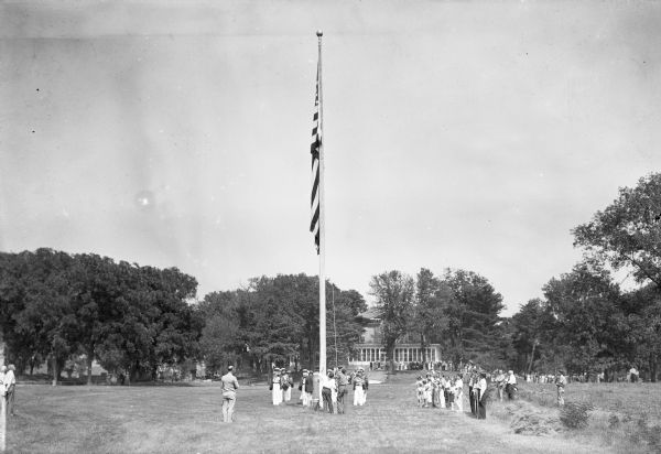 A flag-raising ceremony at Villa Louis, with a group of people standing on the lawn around the flagpole.

