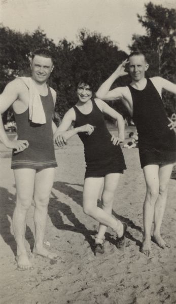 A group of three swimmers, two men and one woman, posing on the beach at Lake Calhoun.