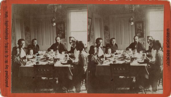 Stereograph of an interior group portrait of eight people sitting around a dining table. Identified as the B.G. Stieg family, the W. Dittberner family, Anna Block, and Reverend Berger.