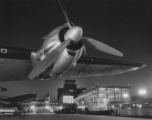 Night view of the air terminal at Mitchell Field. In the foreground is the wing and propeller of a large airplane.