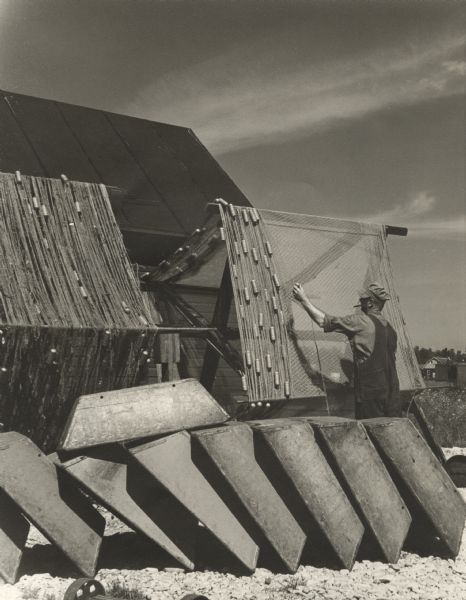 A man preparing nets wound on large reels for fishing. A row of tubs are in the foreground and a shed is in the background.