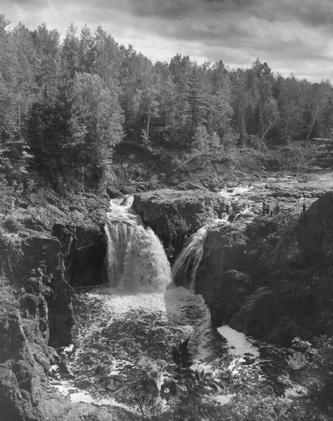 Copper Falls in Copper Falls State Park. The falls are on the Bad River. A group of people are standing on the rocks on the right. Trees are in the background.