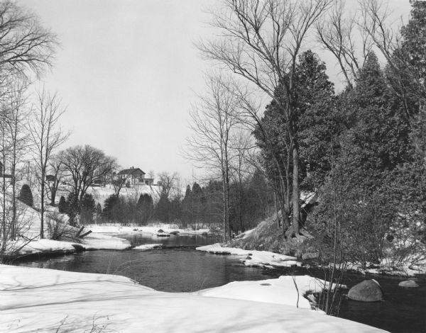 A winter view of the Mullet River near Crystal Lake. In the background is a house on a rise.