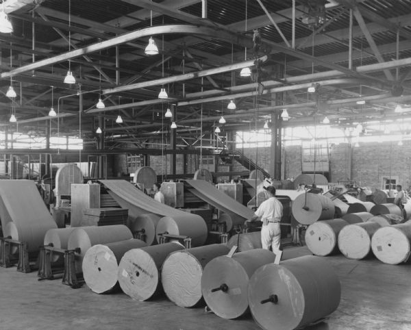Interior view of the Bay West Paper Company with paper converting machinery. Men in uniform are running the equipment.