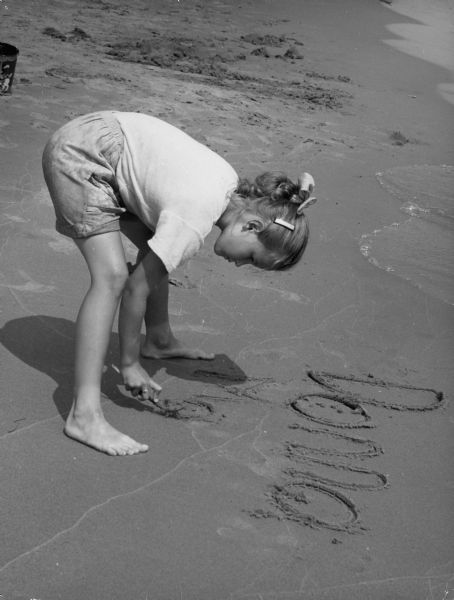Young girl at the beach writing her name in the sand.