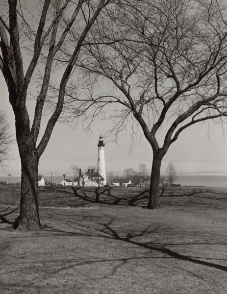 Wind Point Lighthouse surrounded by outbuildings and framed by trees. Lake Michigan is in the distance.