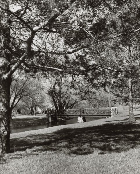 A tree-shaded bridge over a river, probably in a park.