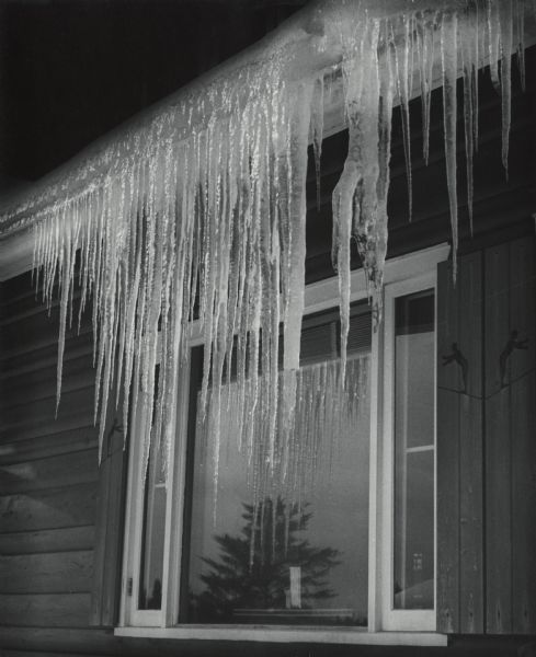 Large icicles hanging in front of a large window from the gutter of a home.