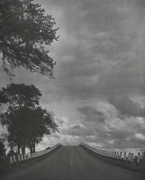 Sky and clouds above Highway 43, west of Kenosha. Guard rails line the highway on both sides and trees can be seen on the left side.