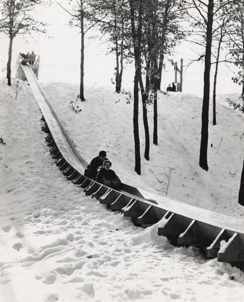 An adult and a child riding a toboggan down the slide at Iverson Park.