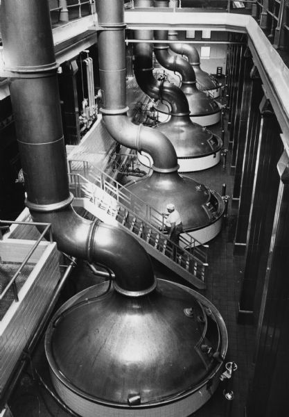 Elevated view of the brewing kettles at the Pabst Brewery. A brewery worker is walking up the stairs in between the kettles.