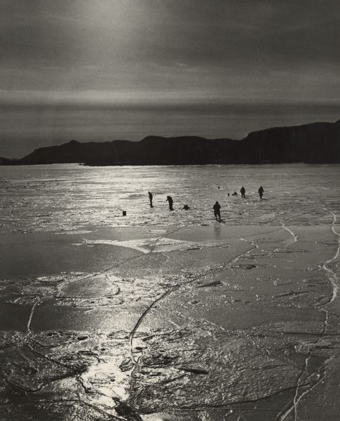 People ice fishing on the frozen Mississippi River. Hills can be seen on the shoreline in the background.