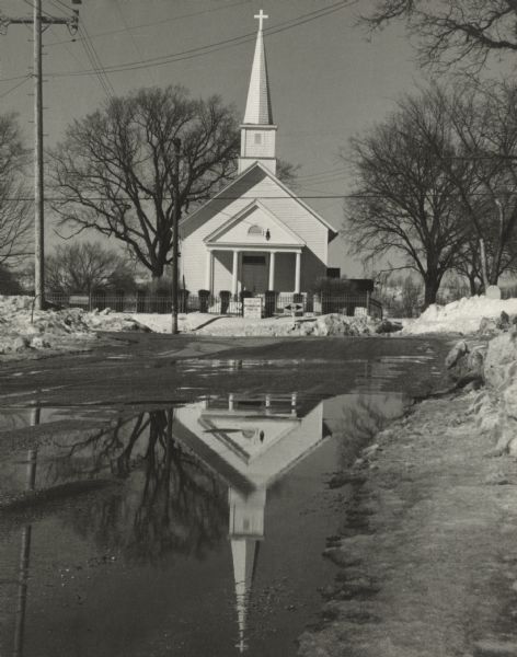 The Stone Bank Presbyterian Church reflected in standing water in springtime. Trees are in the background.