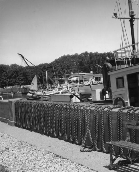 Boats moored at a boat slip. In the foreground is a bench near a concrete wall over which rope is hanging in loops.