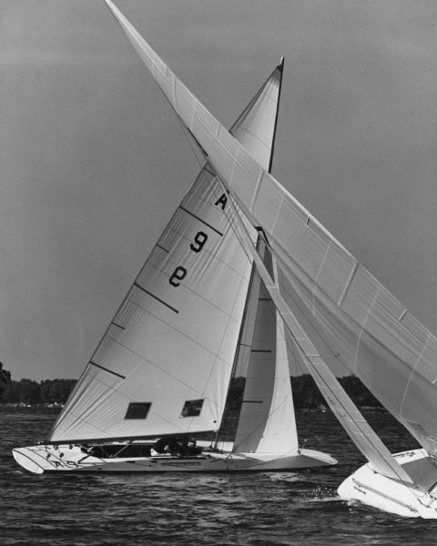 Sailboats "coming about" on Big Cedar Lake. The crew is under the sail of the boat in the center. In the distance is a tree-lined shore.