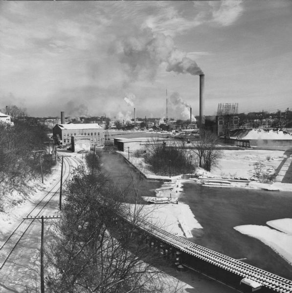Elevated view of the Fox River Valley from Memorial Drive bridge, looking East. Snow is on the ground, ice is on the river and the smokestacks are billowing steam and smoke.