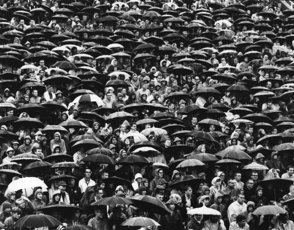 Elevated view of crowd. Umbrellas shelter some spectators sitting in the stands at a football game.