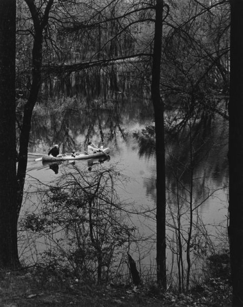 Elevated view from riverbank of a family enjoying a canoe ride on the Wisconsin River, in Tower Hill State Park. The trees are thick on both shorelines.
