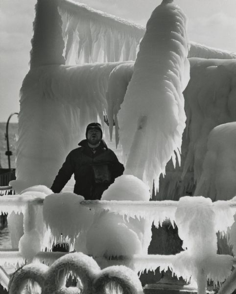 Spray from the lake has built up as thick ice on a ship, creating interesting shapes. A man is standing on the deck.