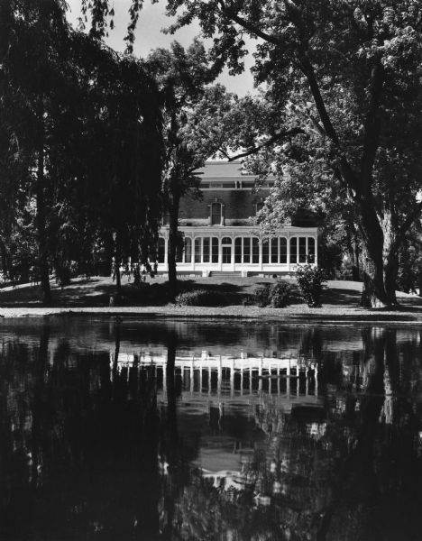 The veranda at Villa Louis reflected in a pond. Many stately trees surround the mansion.