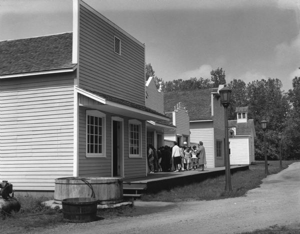 A crowd is standing on the boardwalk in front of a building at Stonefield Village, a Wisconsin Historical Society site.