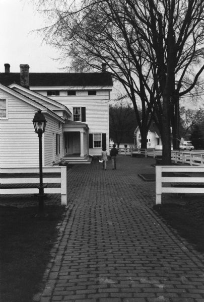 Two people are walking on the brick courtyard at the Old Wade House, a Wisconsin Historical Society site. The Old Wade House, one of the earliest stagecoach inns in Wisconsin, was built between 1847 and 1851 by Sylvanus Wade. It became the most important stop on the plank road between Sheboygan and Fond du Lac.