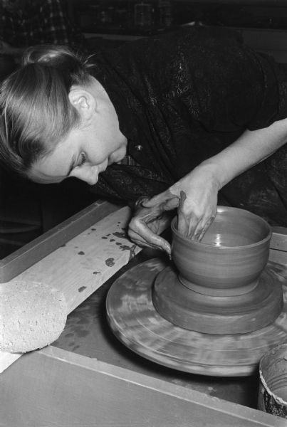 A woman is throwing a pot on the wheel in a pottery class.