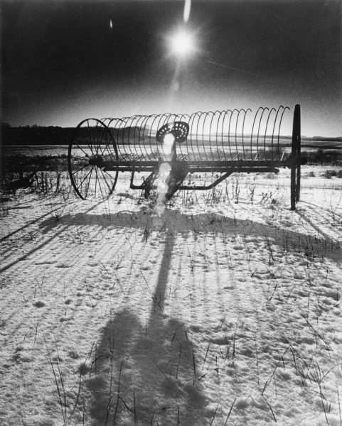 A harrow in a field casting a long shadow on the snow-covered ground.