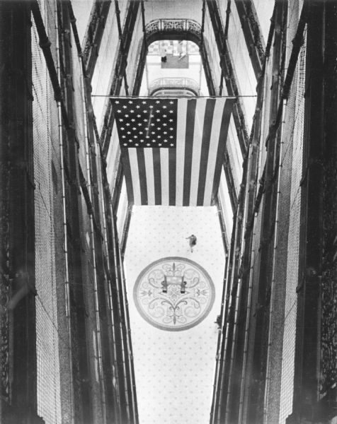 Elevated view of the interior of Milwaukee City Hall. An American Flag is hanging from a pole in the center, and there is an intricate round design on the mosaic floor.